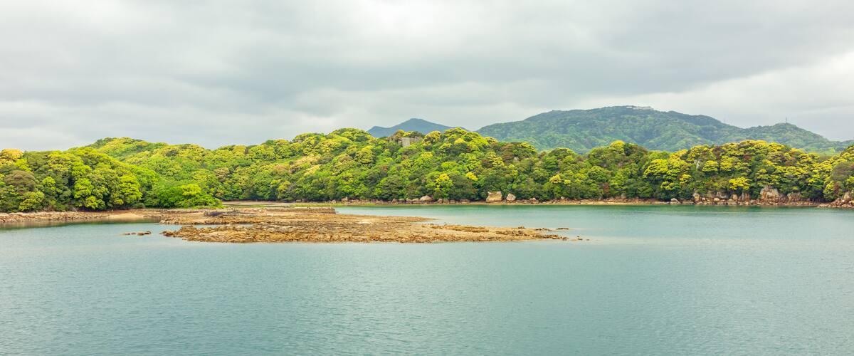 A calm lake surrounded by lush green hills and a cloudy sky.