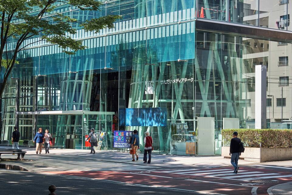 Un bâtiment moderne en verre, avec des personnes qui passent devant.