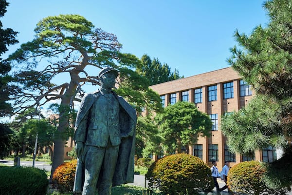 A statue of a man in uniform, a large tree, and a building with multiple windows.