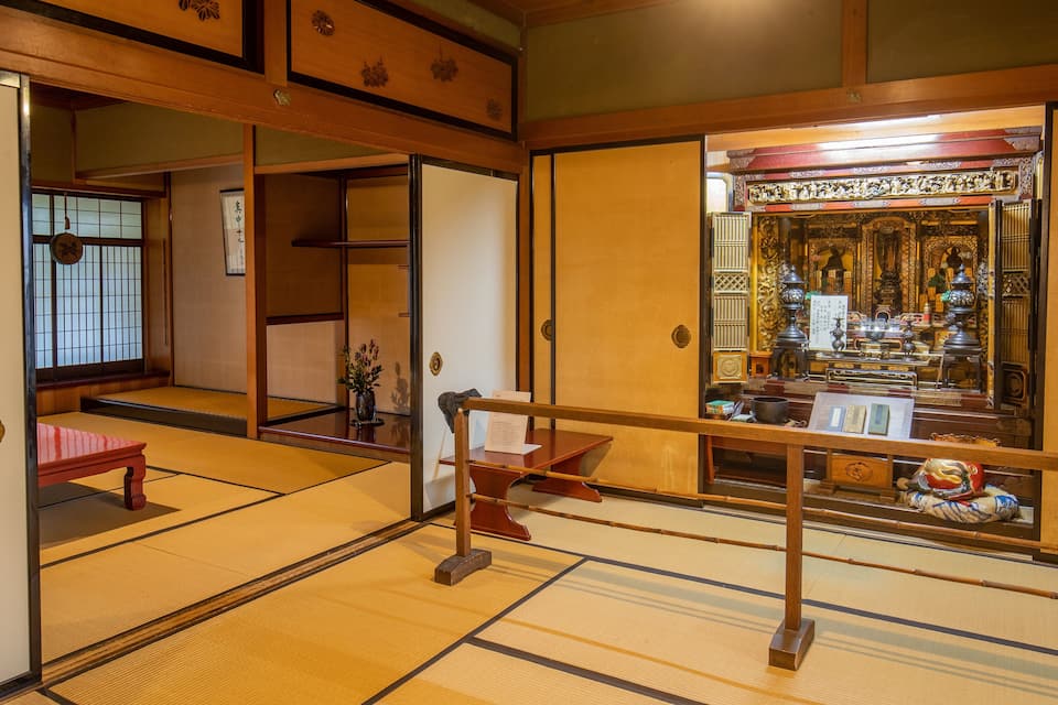 Una stanza tradizionale giapponese con pavimenti in tatami, porte scorrevoli e un'area dedicata a un santuario con oggetti religiosi.