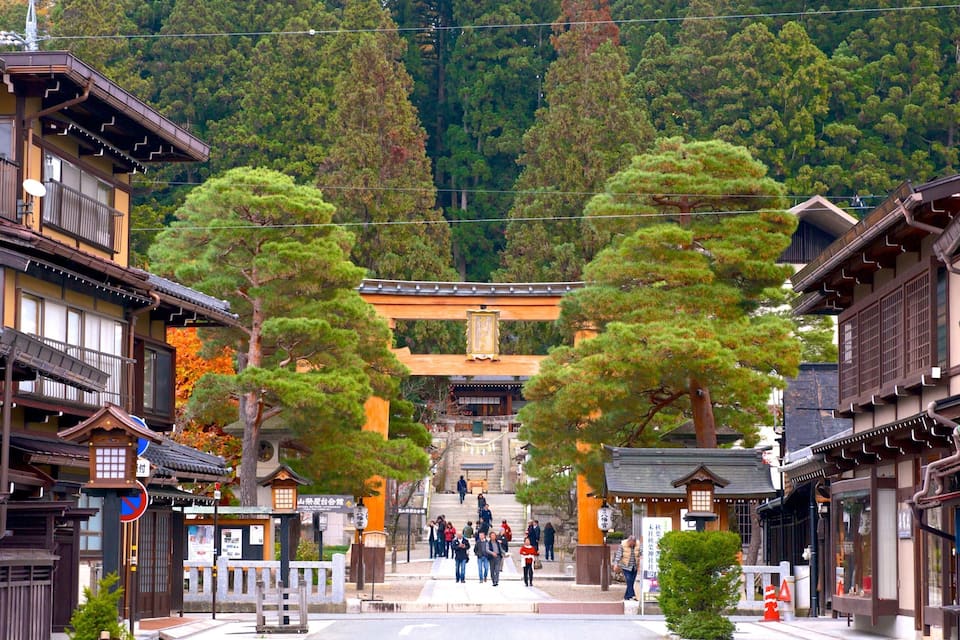 Una strada tradizionale giapponese con edifici in legno, un torii e montagne sullo sfondo.