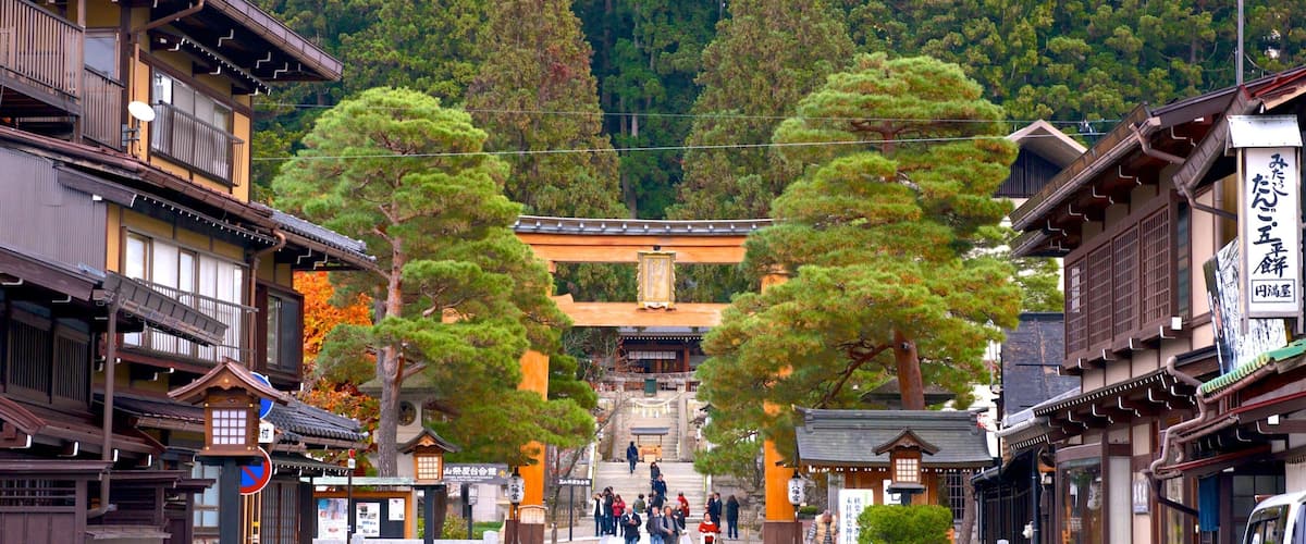 A traditional Japanese street with wooden buildings, a torii gate, and a mountainous backdrop.