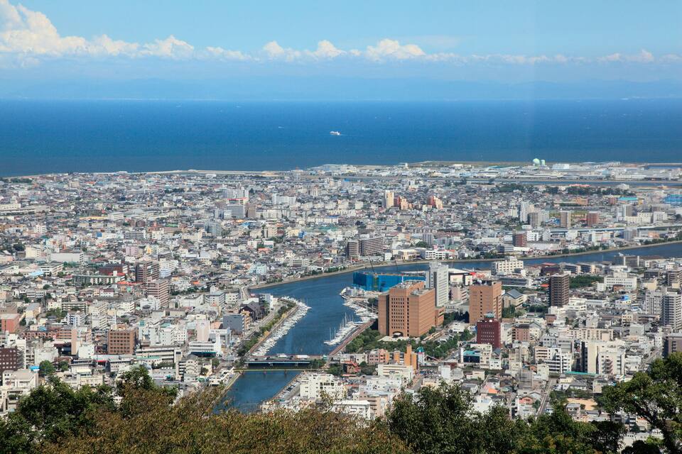 Paisagem urbana costeira com um rio serpenteando por ela, rodeada por edifícios e vista clara do oceano.