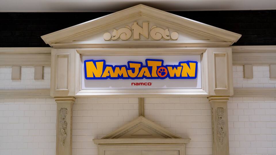 Ein Schild mit 'NamJatown' in fetter Schrift, ein dekorativer Bogen darüber und eine Ziegelwand im Hintergrund.