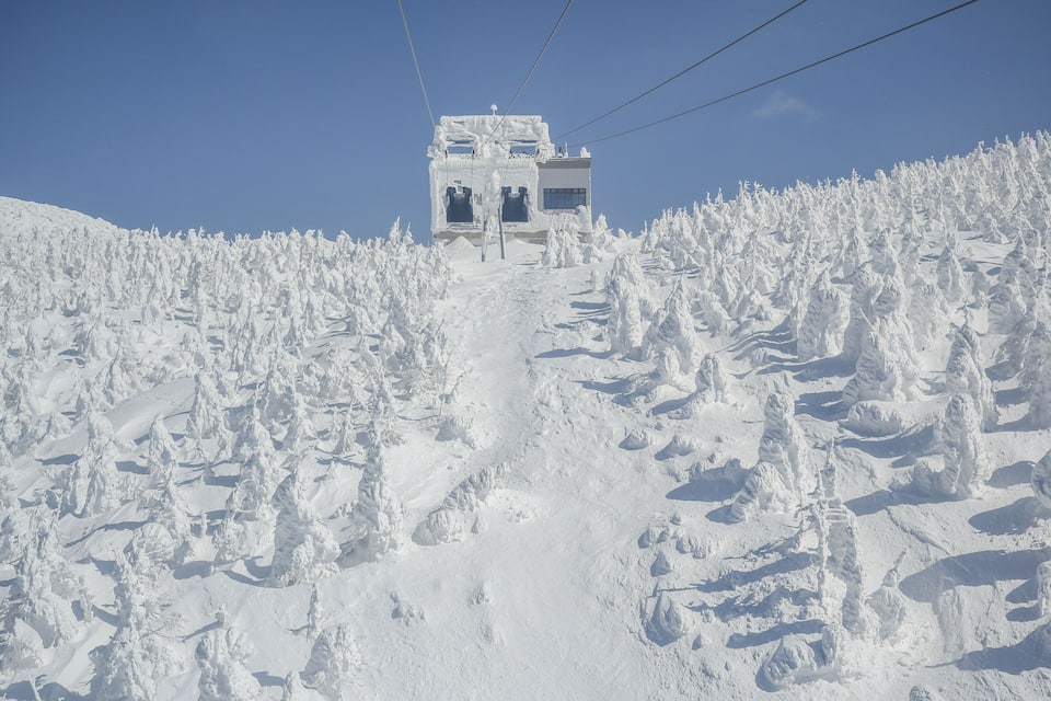 Une montagne enneigée, avec un télésiège, sous un ciel bleu dégagé.