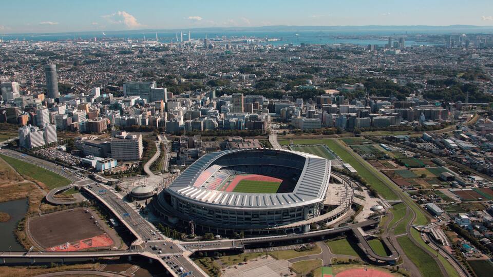 Ein großes Stadion, umgeben von einer Stadtlandschaft mit zahlreichen Gebäuden und einem Fluss im Hintergrund.