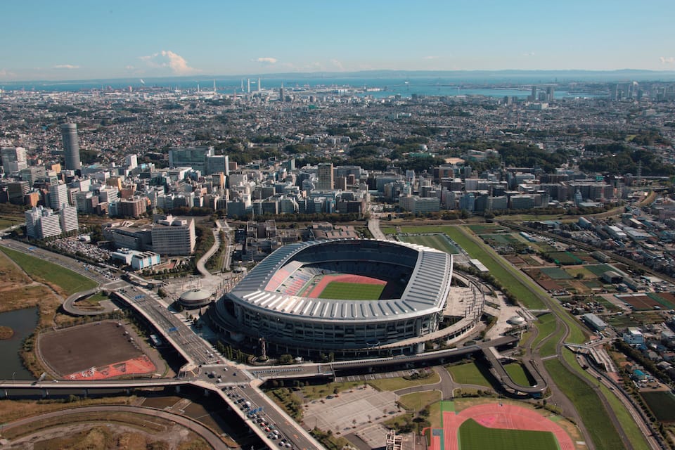 A large stadium surrounded by a cityscape with numerous buildings and a river in the background.