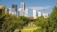 A cityscape with modern skyscrapers, a Ferris wheel, and a park with trees.