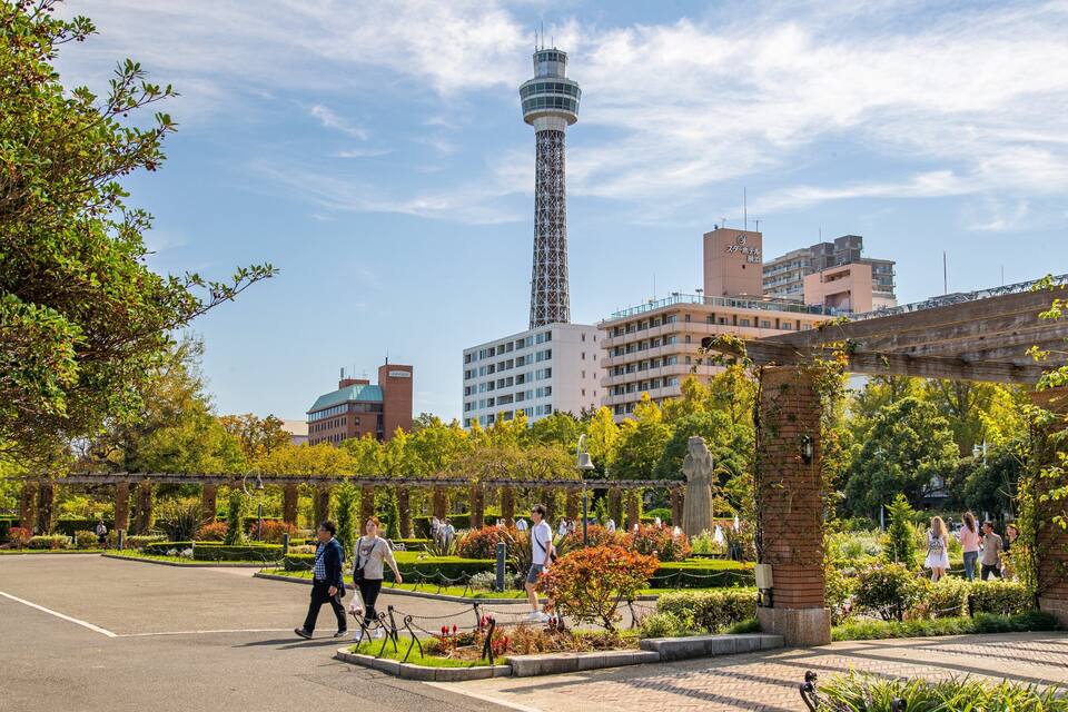 Un parque con una torre alta, un puente y edificios al fondo.