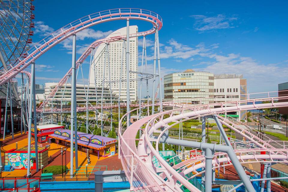 A roller coaster with pink tracks, a Ferris wheel, and a cityscape with modern buildings in the background.