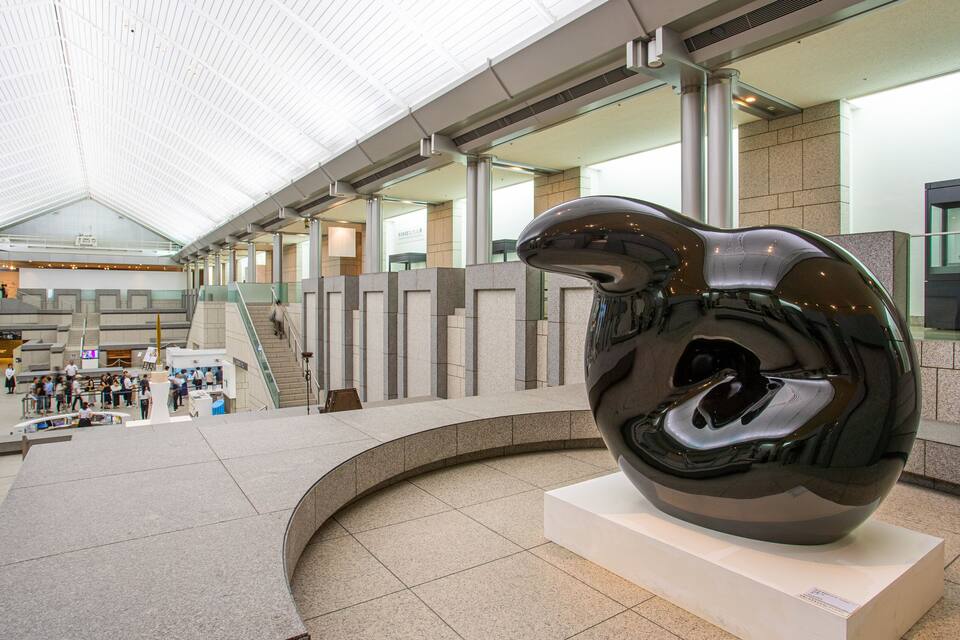 A modern indoor space with a large sculpture, a staircase, and a glass ceiling.