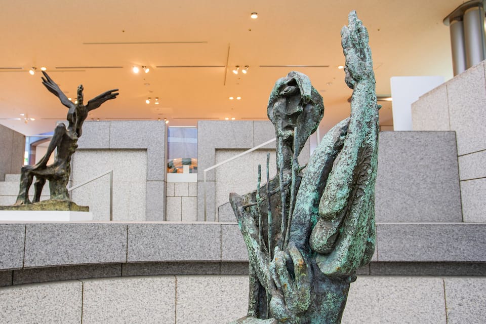Two bronze sculptures in an indoor setting with a stone floor and a staircase in the background.
