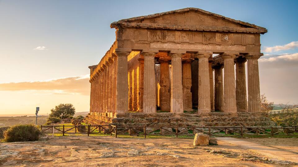 An ancient Greek temple with columns, set against a sunset sky.
