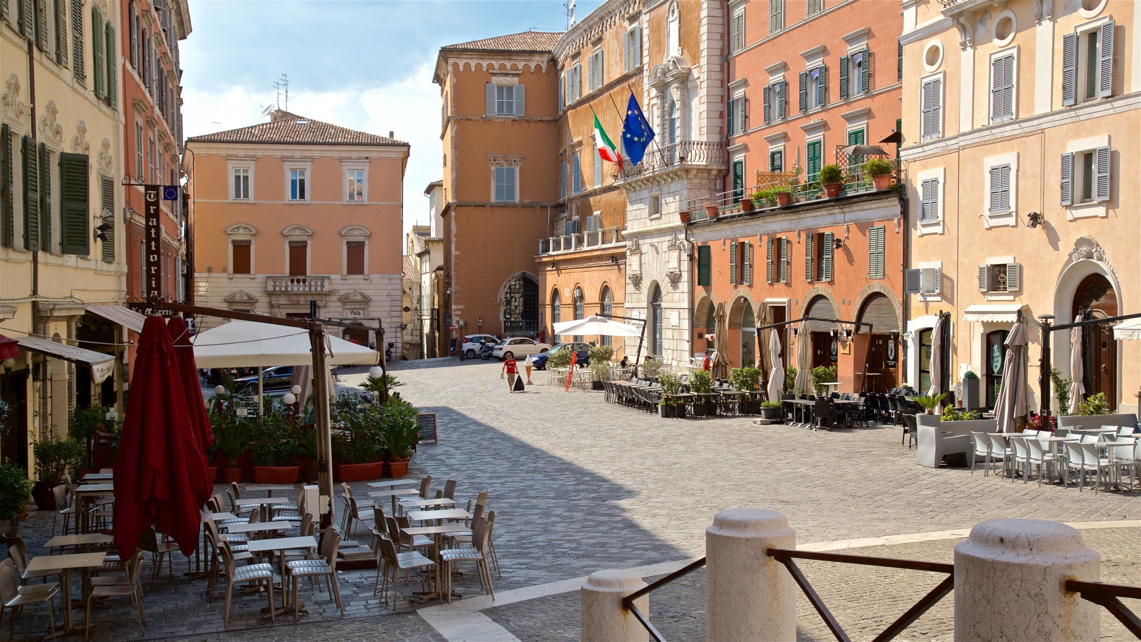 Une rue pavée bordée de cafés en plein air, de bâtiments historiques et de drapeaux.