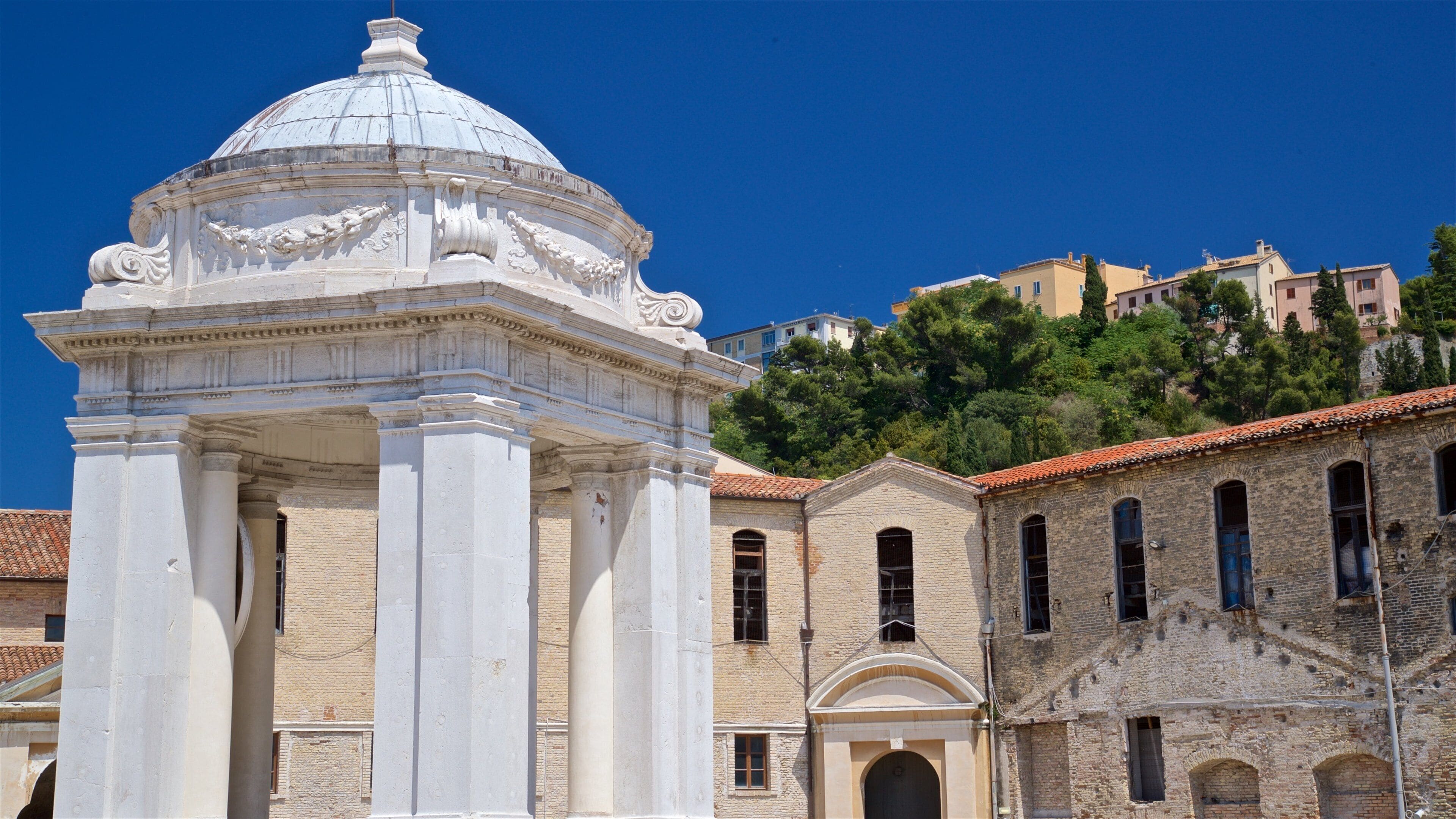 Un bâtiment classique de couleur blanche, doté d’un dôme et de colonnes, situé à côté d’anciens bâtiments en briques avec des fenêtres en arc de cercle.