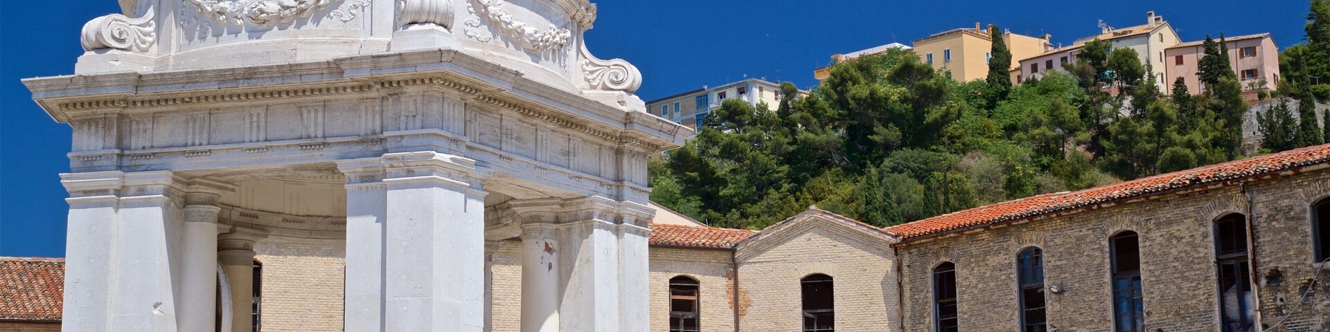 Un edificio clásico blanco con una cúpula y columnas, junto a edificios de ladrillo más antiguos con ventanas arqueadas.