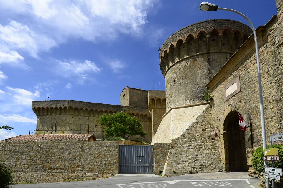 A historic stone building with a round tower, a metal gate, and a street sign.