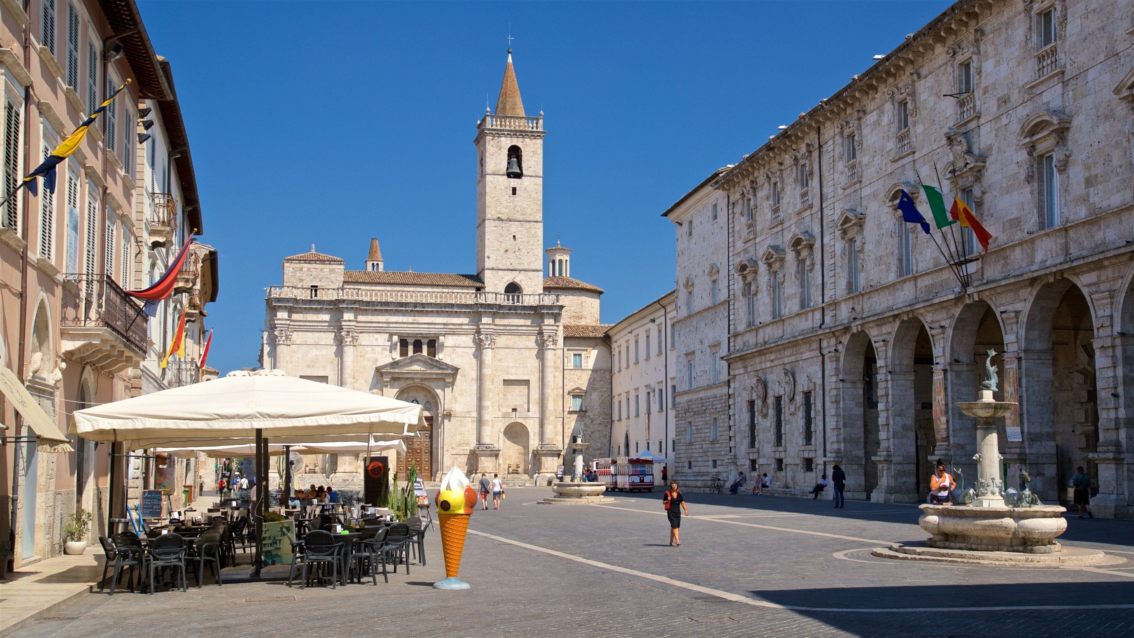 A historic square with a prominent church tower, outdoor seating, and a fountain.