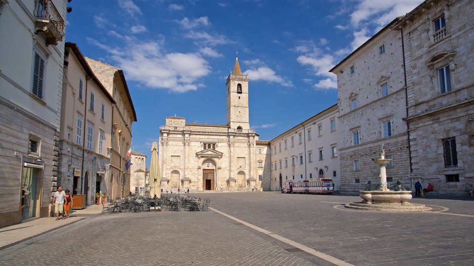 A cobblestone square with historic buildings, a prominent church with a bell tower, and a fountain.
