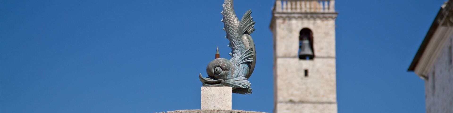 A fountain with a mermaid statue in front of a historic building with a bell tower.