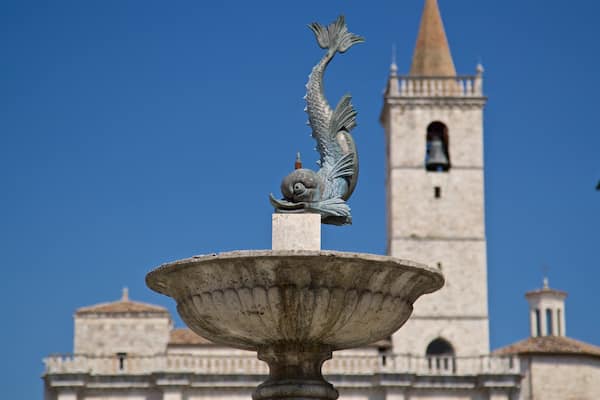 Une fontaine ornée d’une statue de sirène, située devant un bâtiment historique doté d’un clocher.