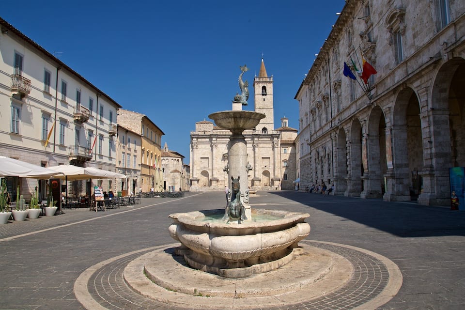 A historic square with a central fountain, surrounded by classical architecture and outdoor seating areas.