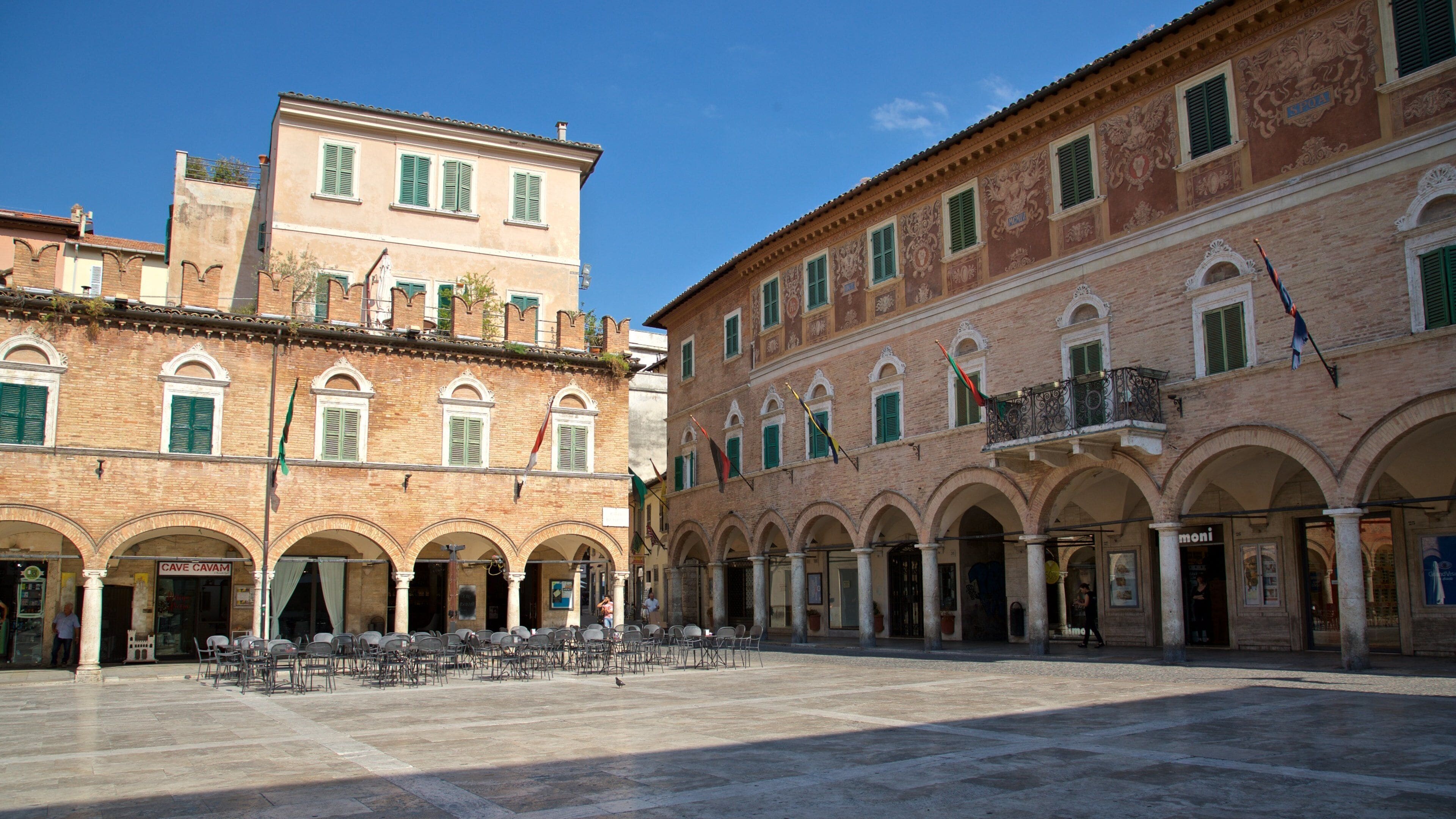 A historic square with classical architecture, featuring arches, columns, and a variety of buildings with distinct facades.