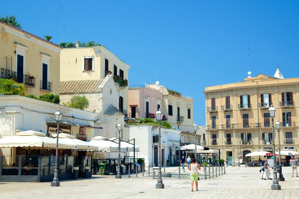 A sunny square with historic buildings, outdoor cafes, and a clear blue sky.