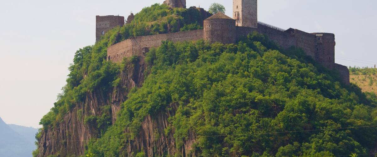 A medieval castle atop a lush green hill with multiple towers.