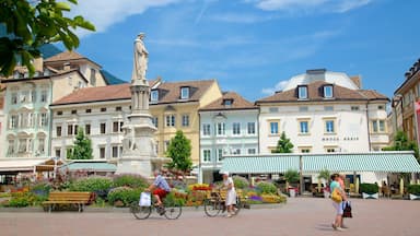 Uma praça urbana com uma estátua, edifícios coloridos e um hotel chamado 'Hotel Greif'.