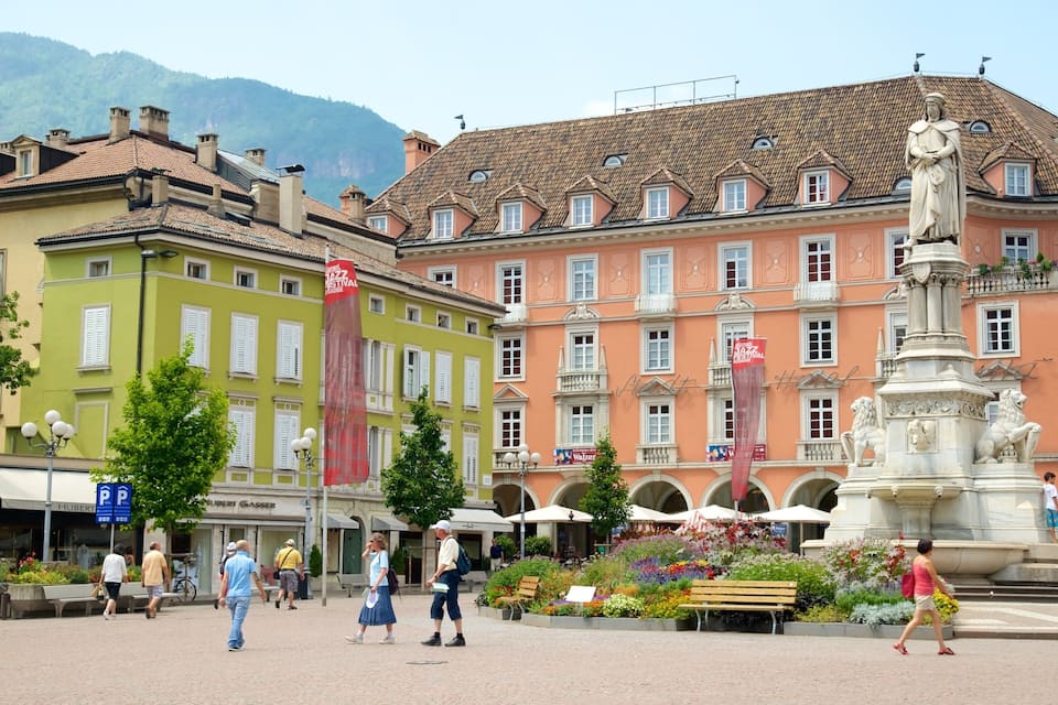 A public square with a statue, colorful buildings, and a mountain in the background.