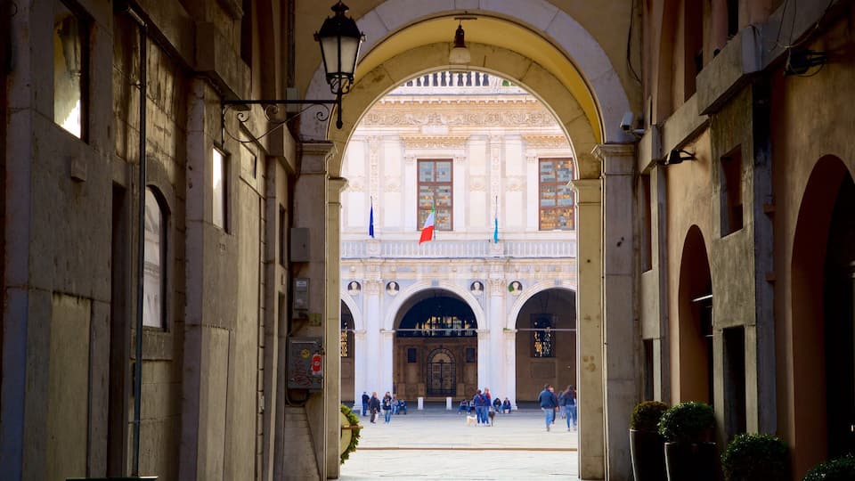 An arched passageway leading to a historic building with ornate architecture and flags.
