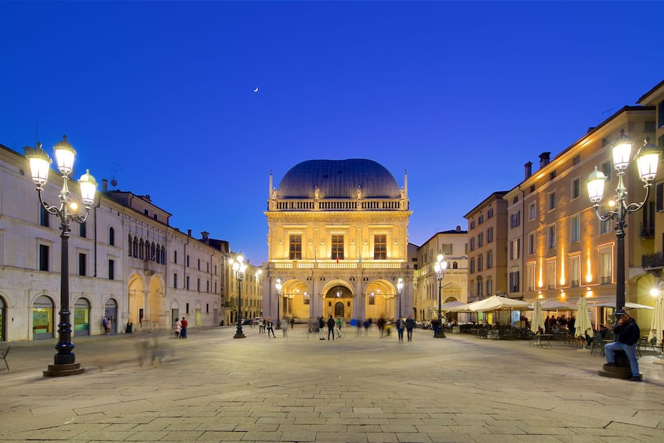 Ein historischer Platz mit einem markanten Gebäude, das eine Kuppel und klassische Architektur aufweist, umgeben von beleuchteten Straßen und Cafés.