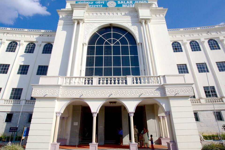 A large white building with a central arched window, columns, and a sign reading "Salar Jung Museum".