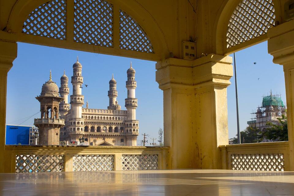A historic building with multiple domes and minarets, viewed through a yellow structure with lattice windows.