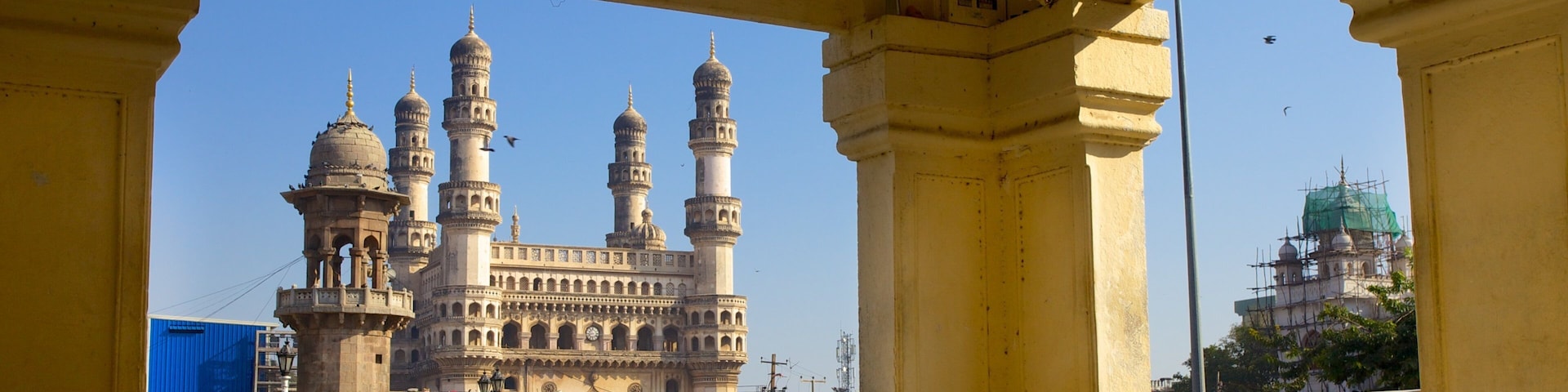 A historic building with multiple domes and minarets, viewed through a yellow structure with lattice windows.