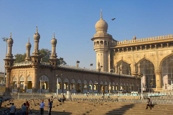 A large mosque with multiple domes and minarets, surrounded by a white fence and steps leading up to it.
