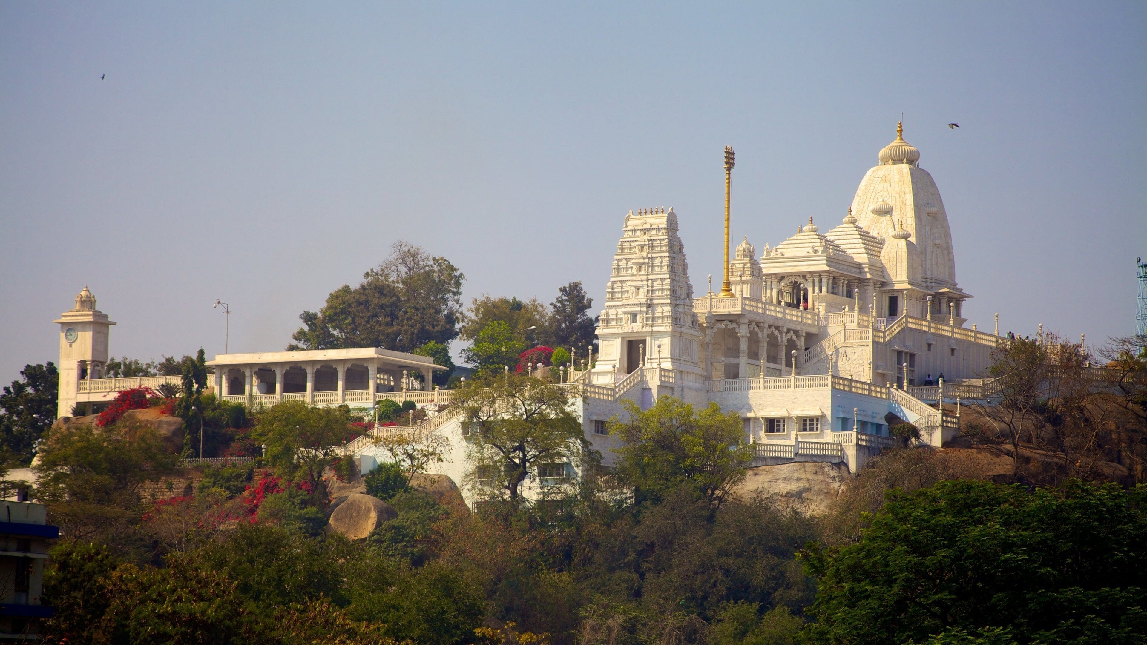 A large white temple complex with intricate architecture, surrounded by lush greenery and trees.