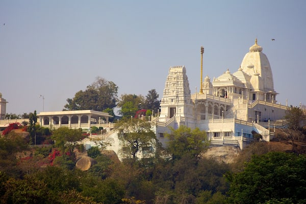 A large white temple complex with intricate architecture, surrounded by lush greenery and trees.