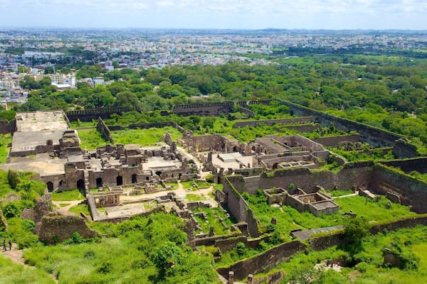 An ancient fortress surrounded by lush greenery, with a cityscape in the background.