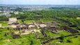An ancient fortress surrounded by lush greenery, with a cityscape in the background.