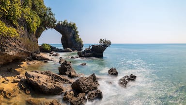 Paisagem costeira com um arco rochoso imponente, águas azul-claras e vegetação exuberante.