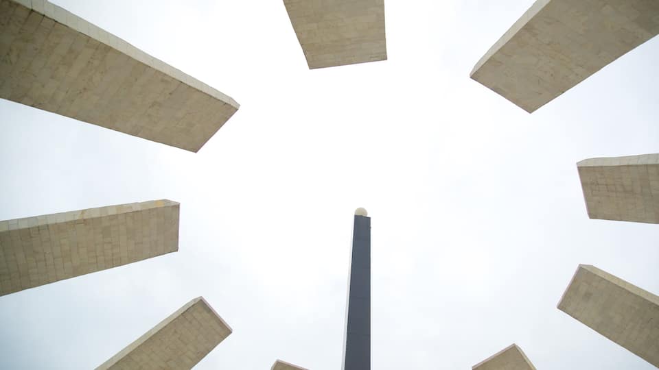 Uma torre alta e estreita, rodeada por edifícios grandes e retangulares.