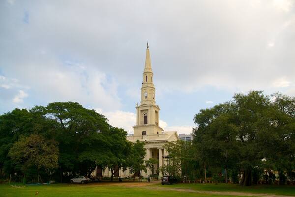 Une église imposante, dotée d’une flèche, entourée d’arbres et bordée d’une pelouse.