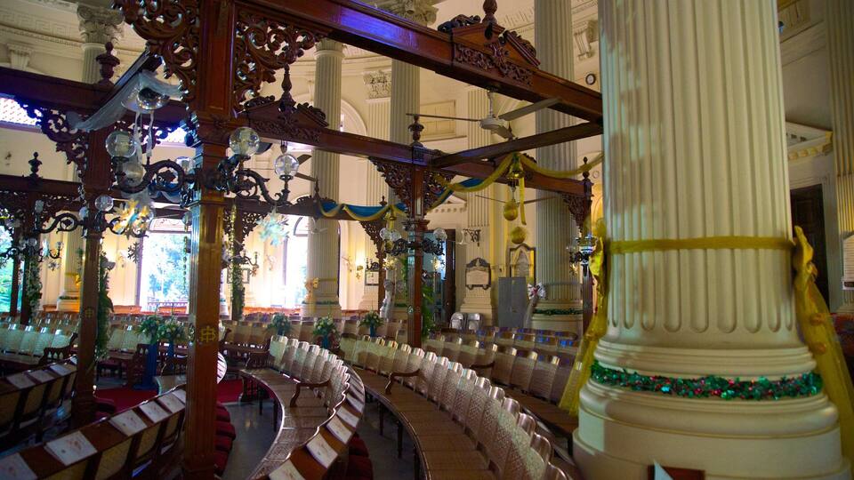 An ornate church interior with rows of pews, a large white column, and decorative chandeliers.
