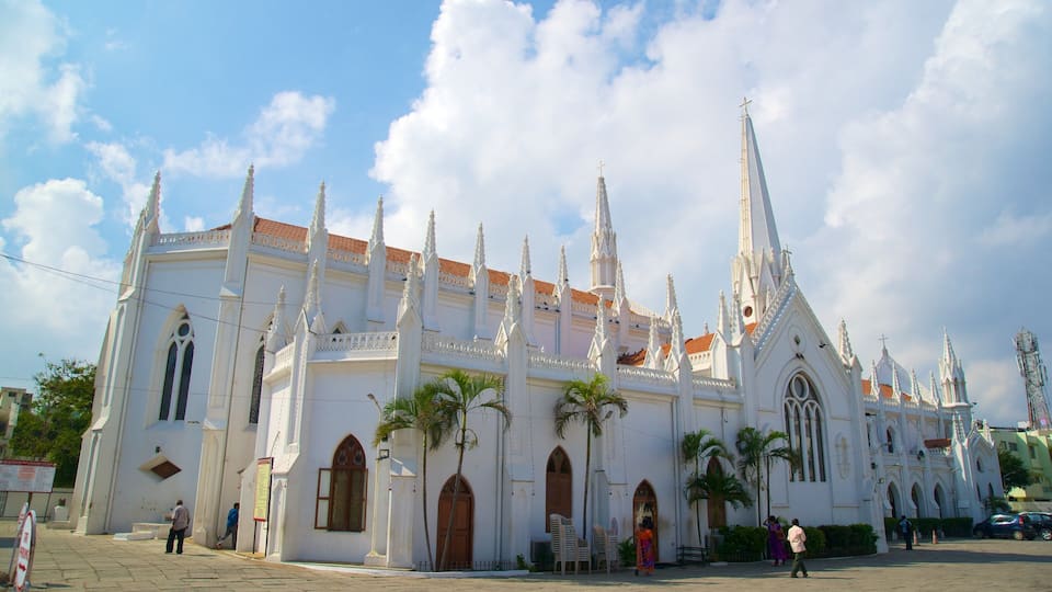 Una iglesia blanca con múltiples torres y una cruz en la parte superior, rodeada de palmeras y gente.
