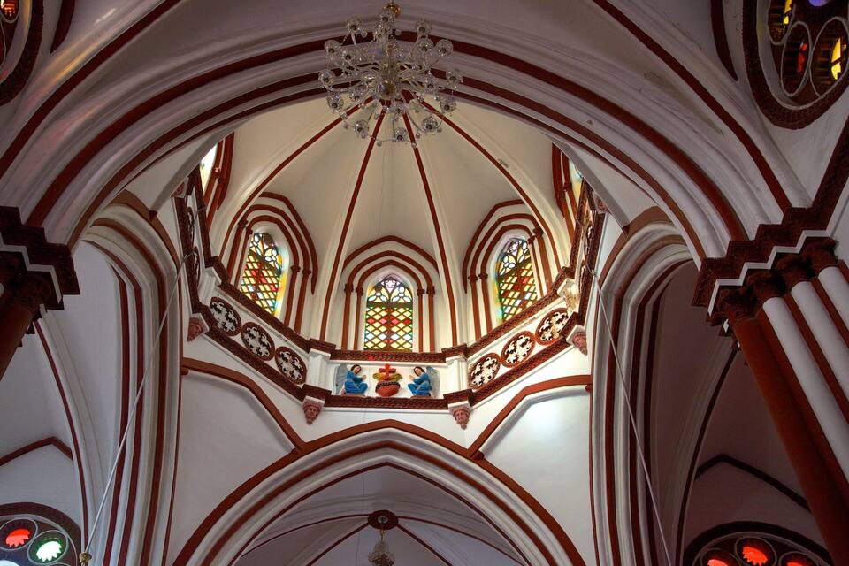 A church interior with a large chandelier, stained glass windows, and red and white architectural details.