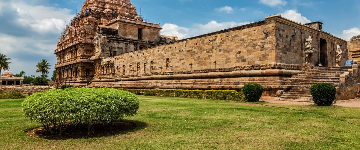 A historic temple with a large spire, a stone building with sculptures, and a well-maintained lawn.