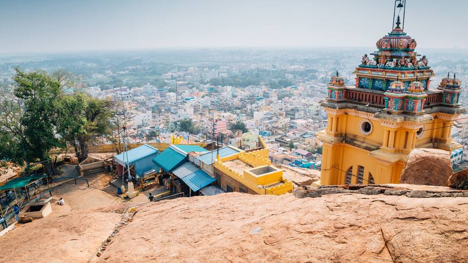 A temple with intricate architecture, a rocky foreground, and a cityscape in the background.