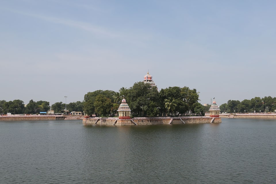 A temple complex with a central tower surrounded by smaller structures, set against a backdrop of trees and a clear sky.